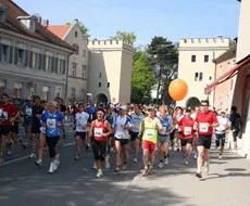 A group of runners in athletic clothing running down a city street, with some holding an orange balloon.