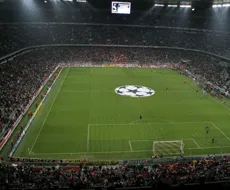 A football stadium with a large display screen and a logo at the center of the field.