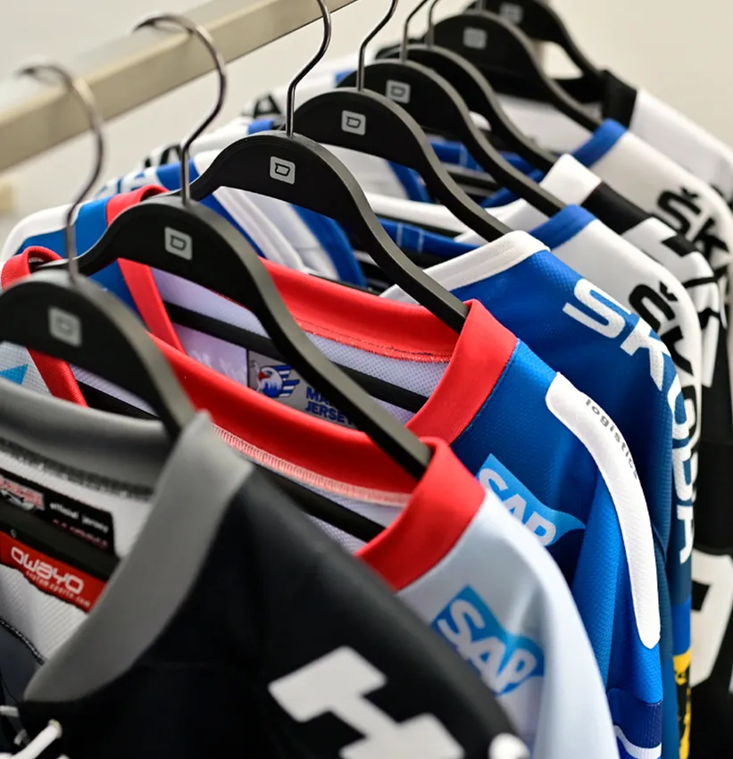 A row of colorful, customized sportswear jerseys from owayo hangs on black hangers on a clothing rack.
