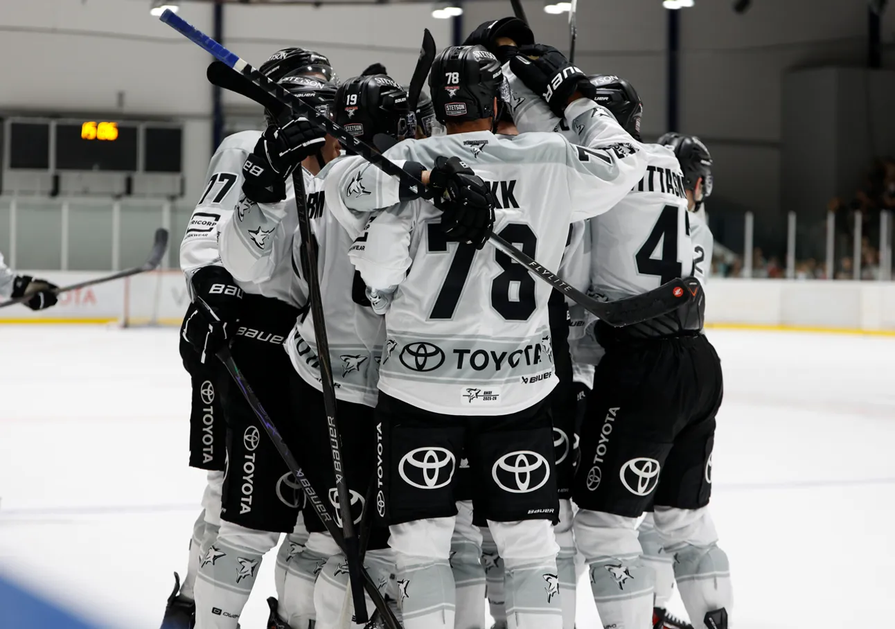Hockey players in white jerseys with black numbers and sponsor logos hugging on the ice.