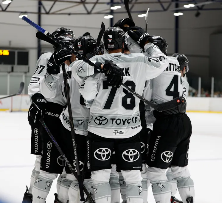 Hockey players in white jerseys with black numbers and the Toyota logo celebrate on the ice.