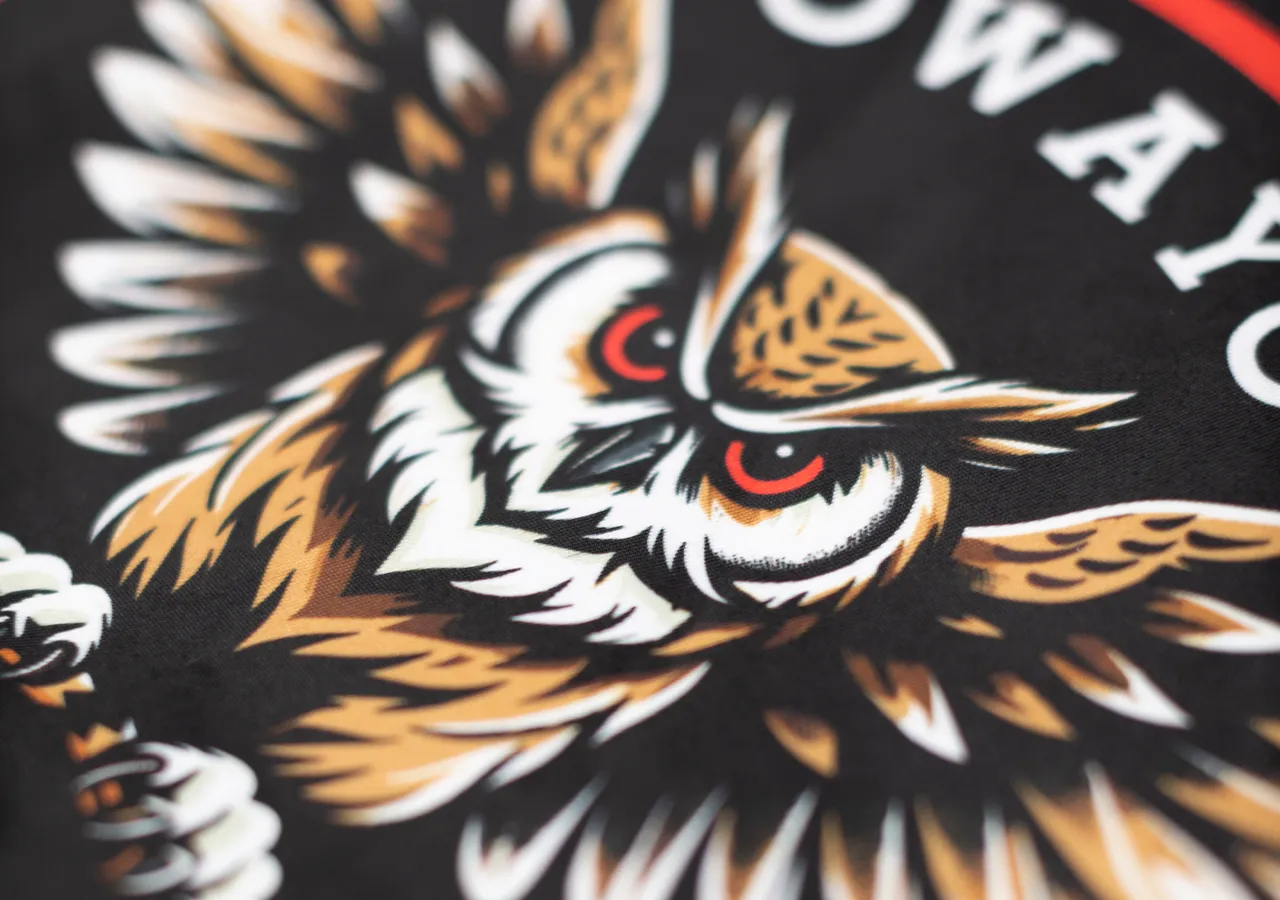 Close-up of a detailed owl design on black fabric, symbolizing strength and dynamism.