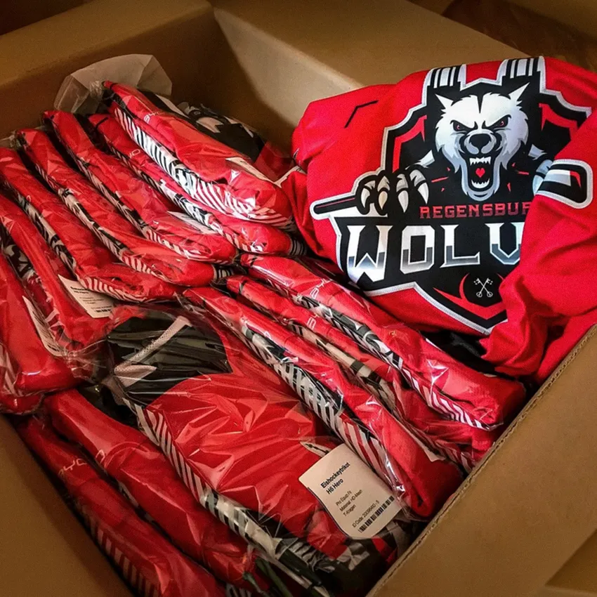 A box filled with red sportswear featuring a wolf logo and various clothing items wrapped in transparent packaging.