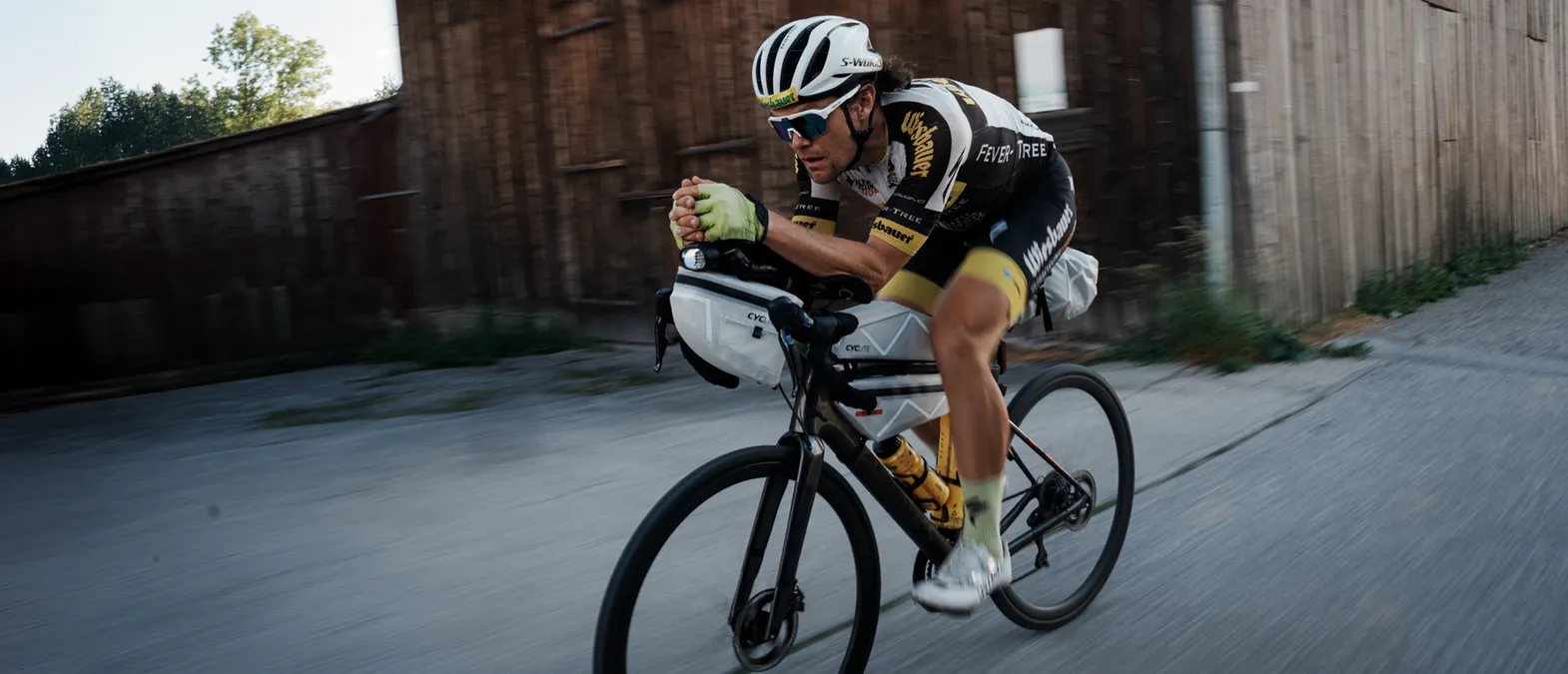 A cyclist in an aerodynamic position on a road bike, wearing customized sportswear from owayo, riding on a street.