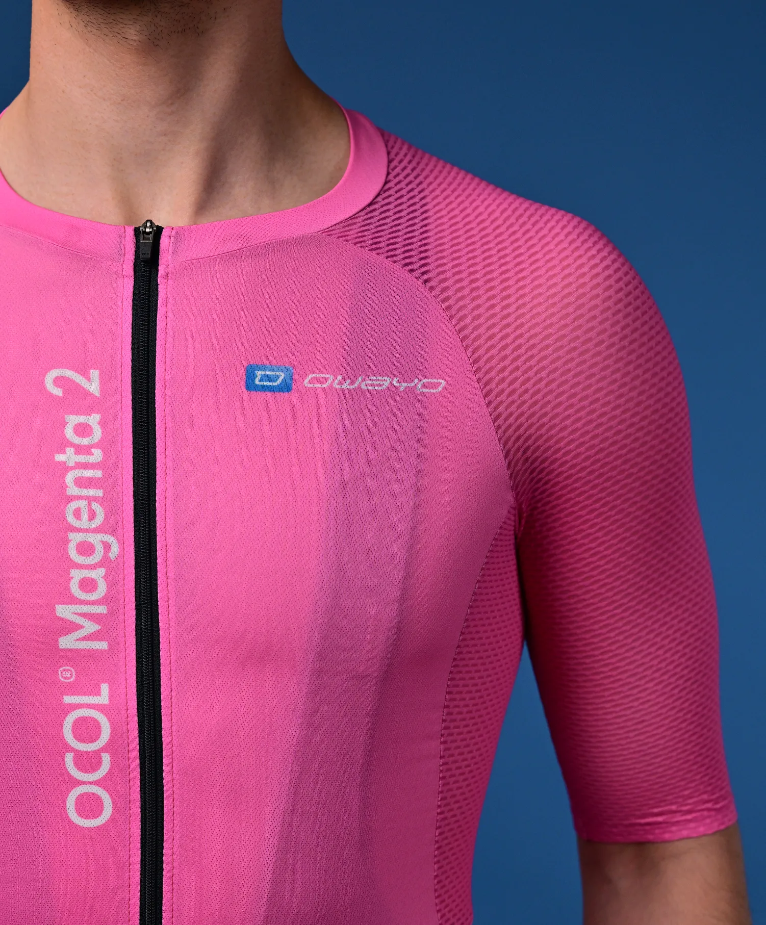 A man wears a pink, short-sleeved cycling jersey with a black zipper and the 'owayo' logo on the chest. Vertically on the left side, it says 'OCOL Magenta 2'.