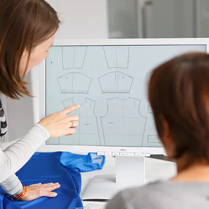 Two people are looking at digital sportswear patterns on a computer screen, with one person pointing at the screen.