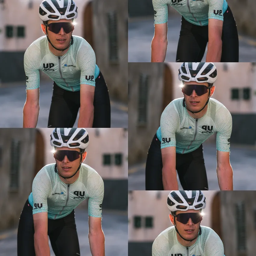 A cyclist in a light blue short-sleeve jersey and sunglasses riding a bike in an urban setting.