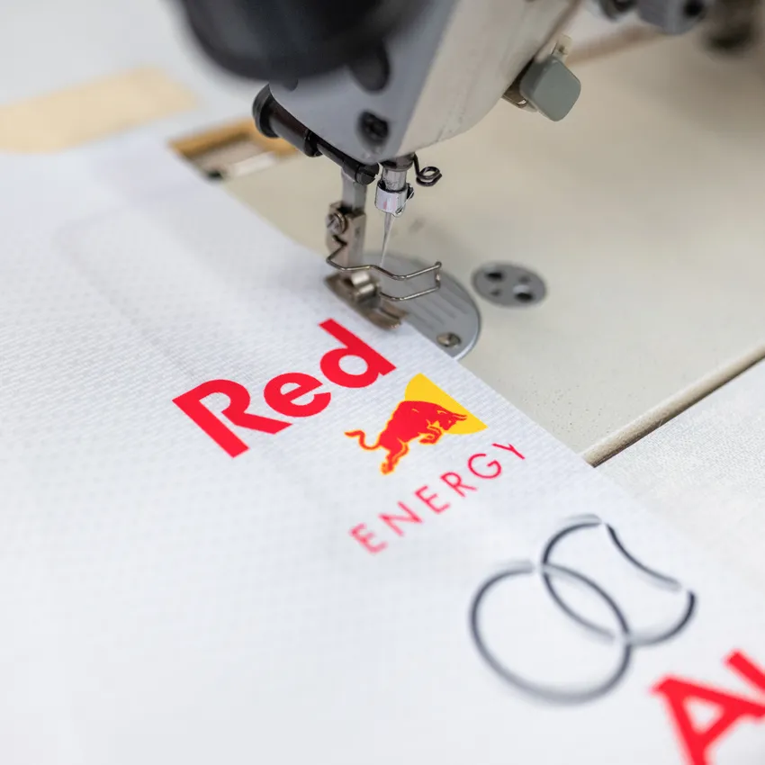A sewing machine stitching onto white fabric featuring colorful logos.