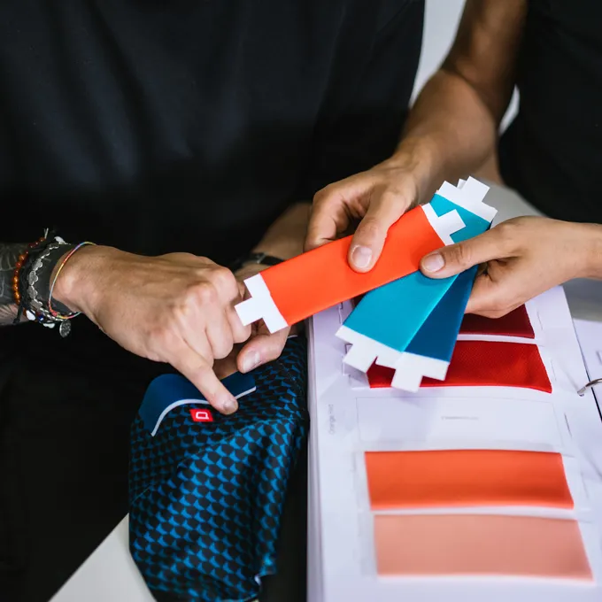 Two people select color swatches for customized sportswear, with a blue patterned fabric and various color options visible.